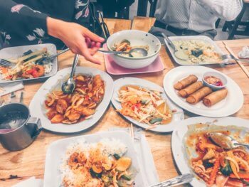 Table full of Thai food with hand reaching for rice